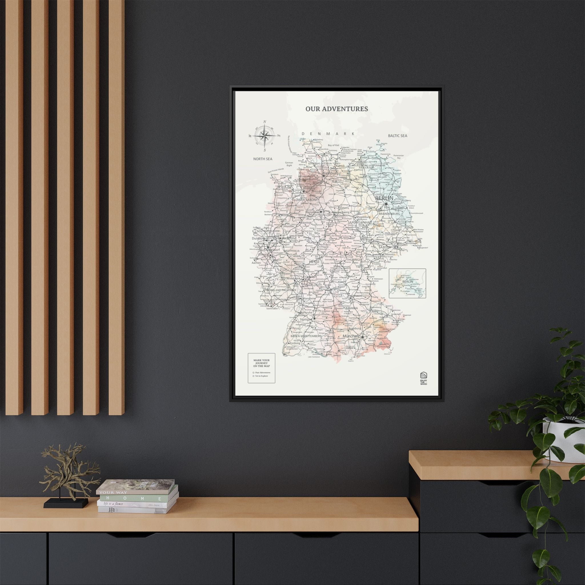 Framed map titled 'Our Adventures' on a dark wall with wooden furniture and plants.