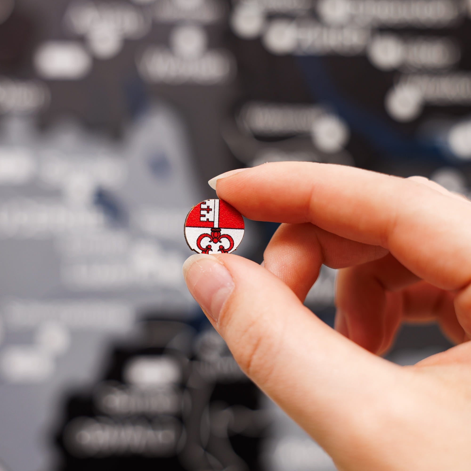 Hand holding a small round badge with a logo against a blurred background of text and logos.