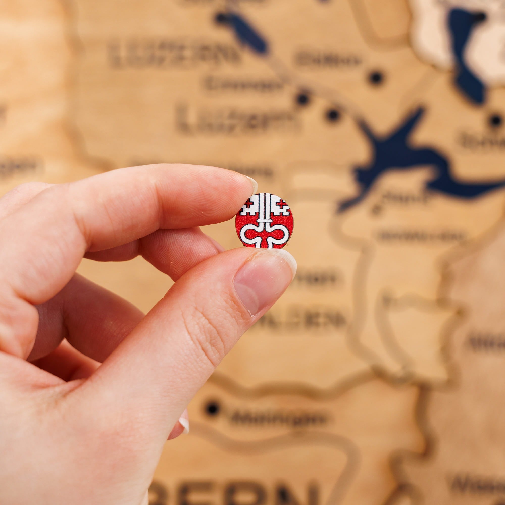 Hand holding a small round red and white object with a logo against a blurred map background