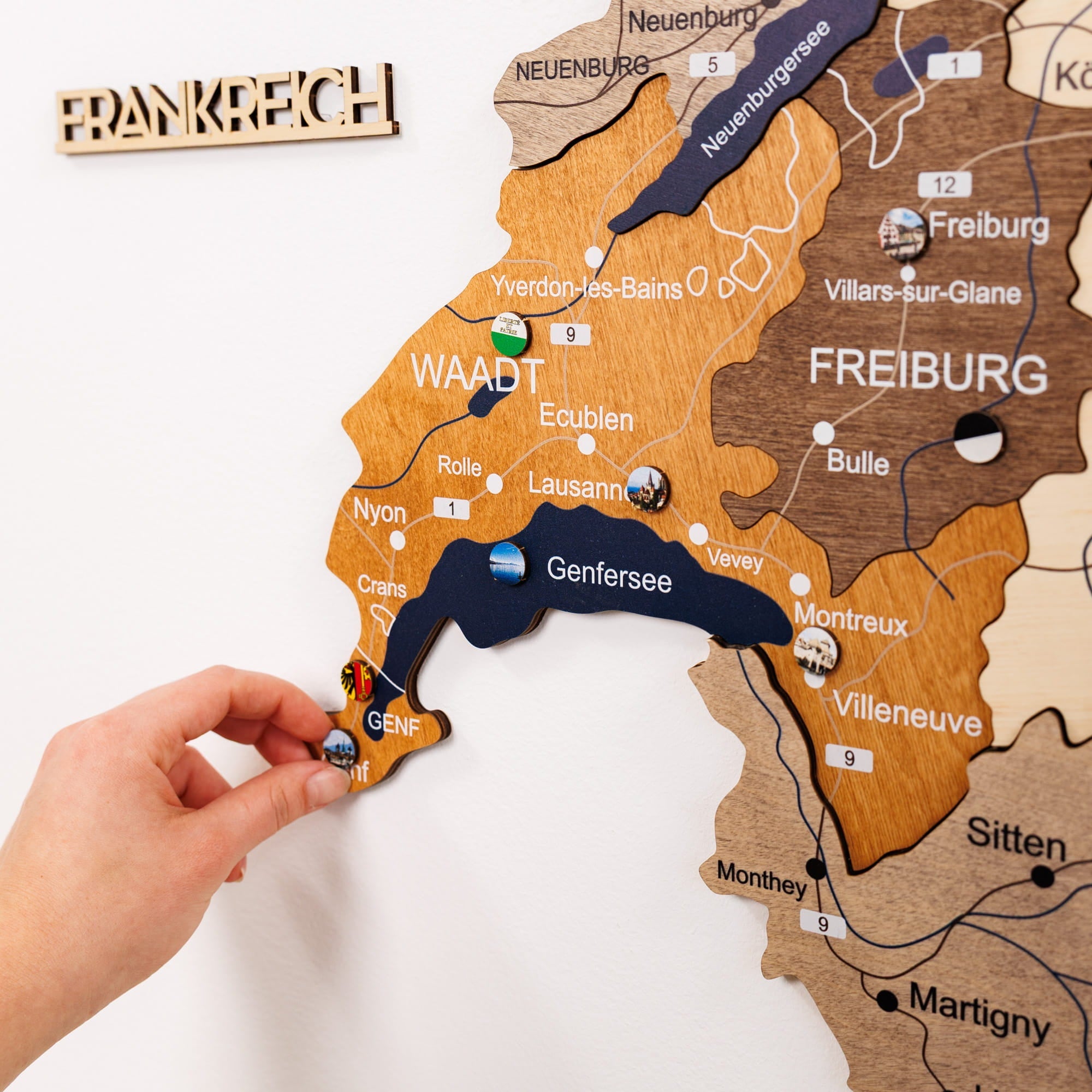 Wooden map of Switzerland with a hand placing a small flag on it.
