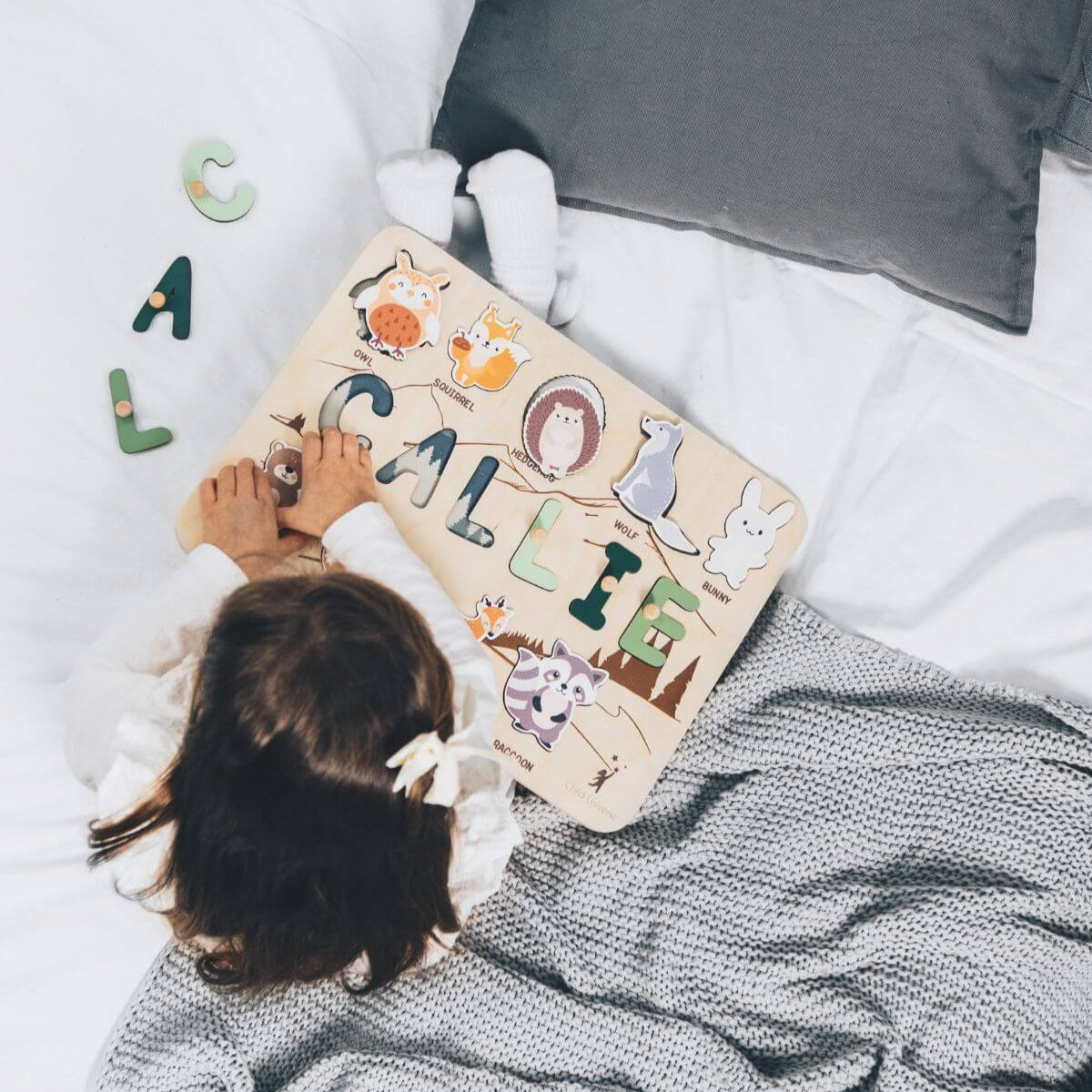 Child playing with a wooden name puzzle on a bed
