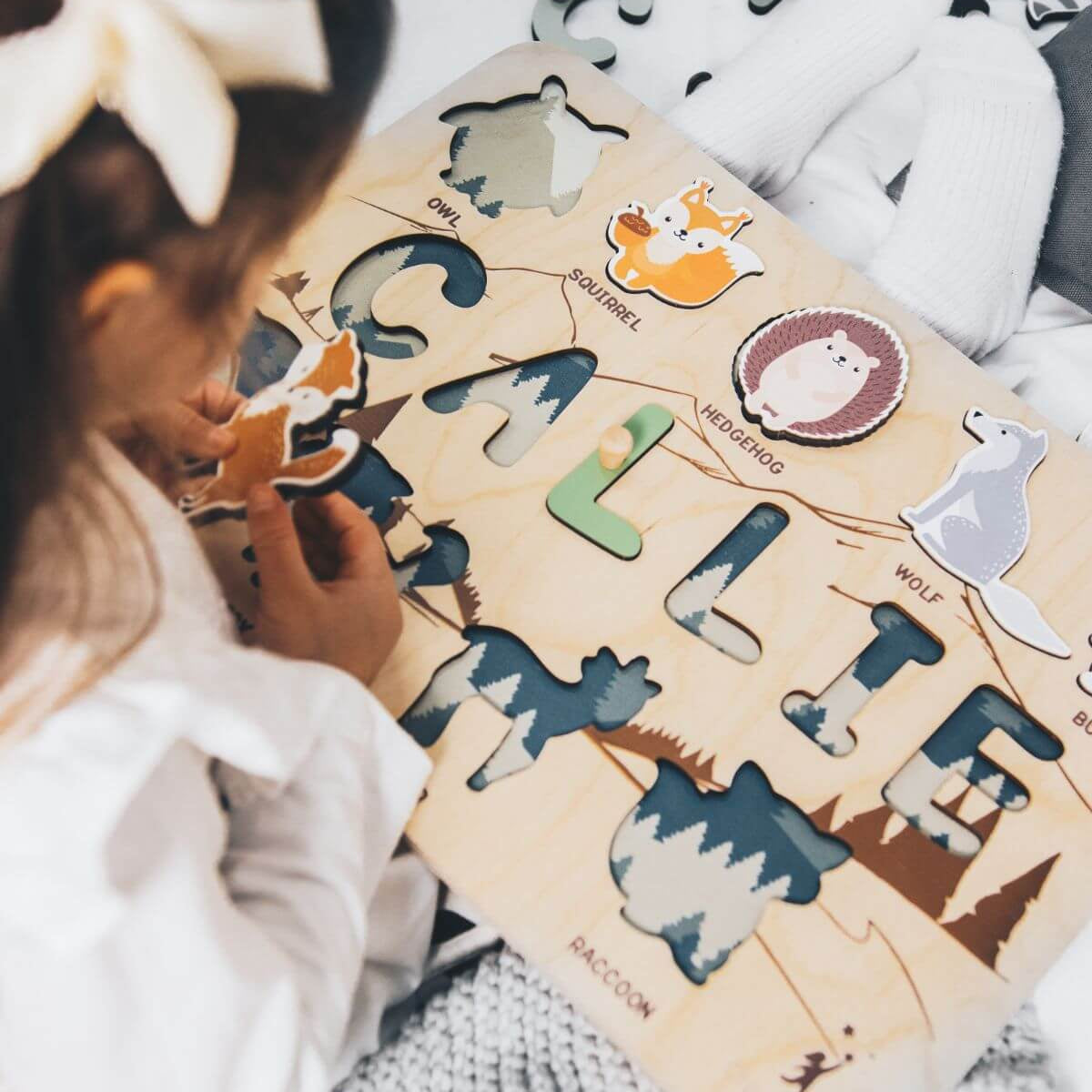 Child playing with a wooden puzzle featuring animal shapes and letters.