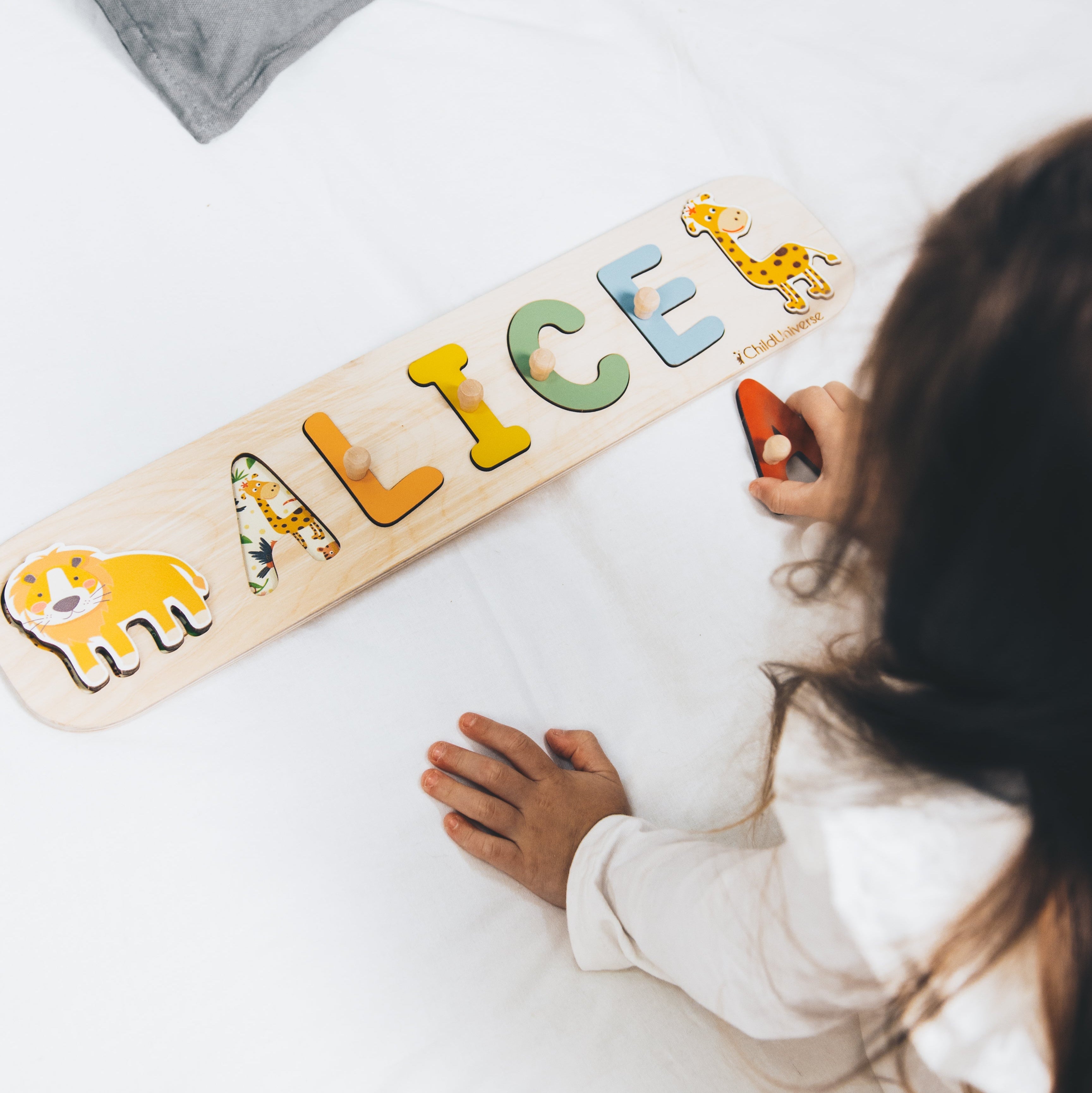 Child playing with a wooden name puzzle spelling 'ALICE' on a white surface.