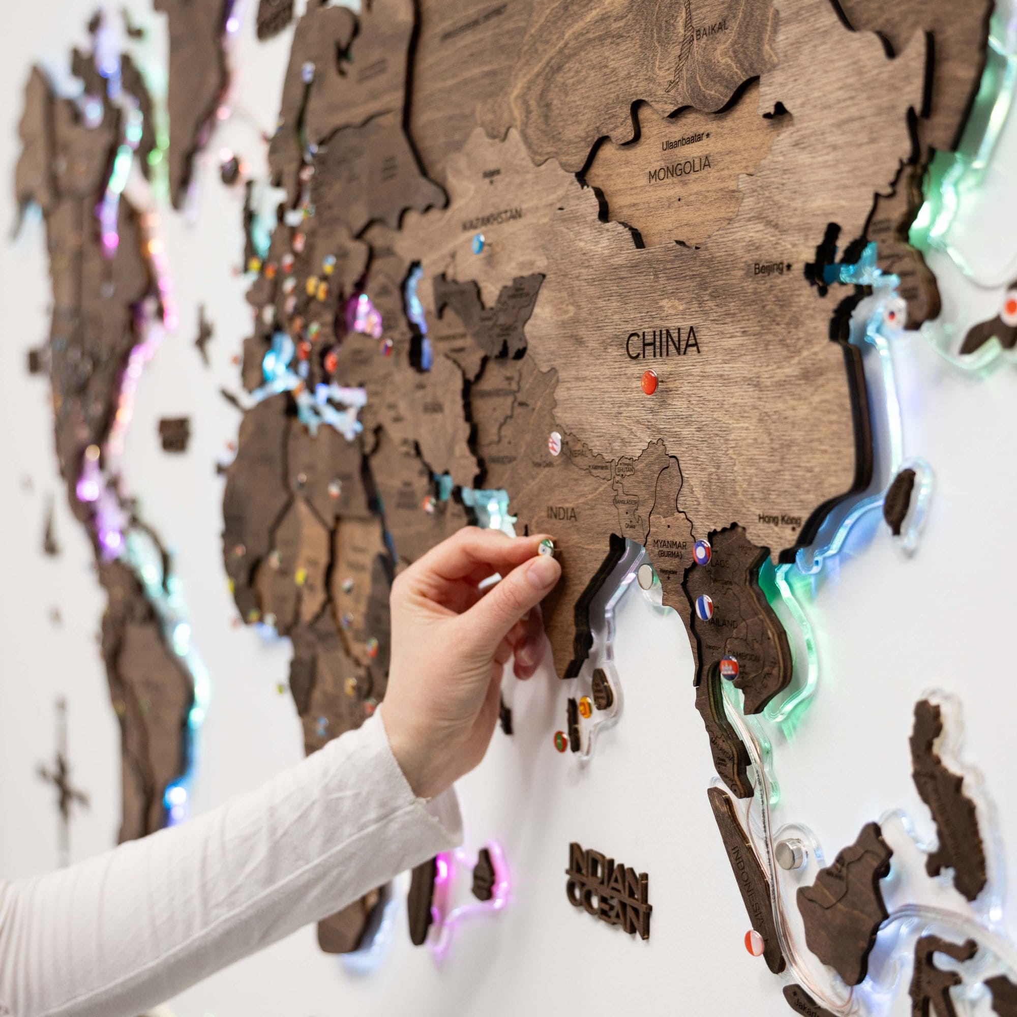 Wooden world map with LED lighting, showing a hand placing a pin on China.