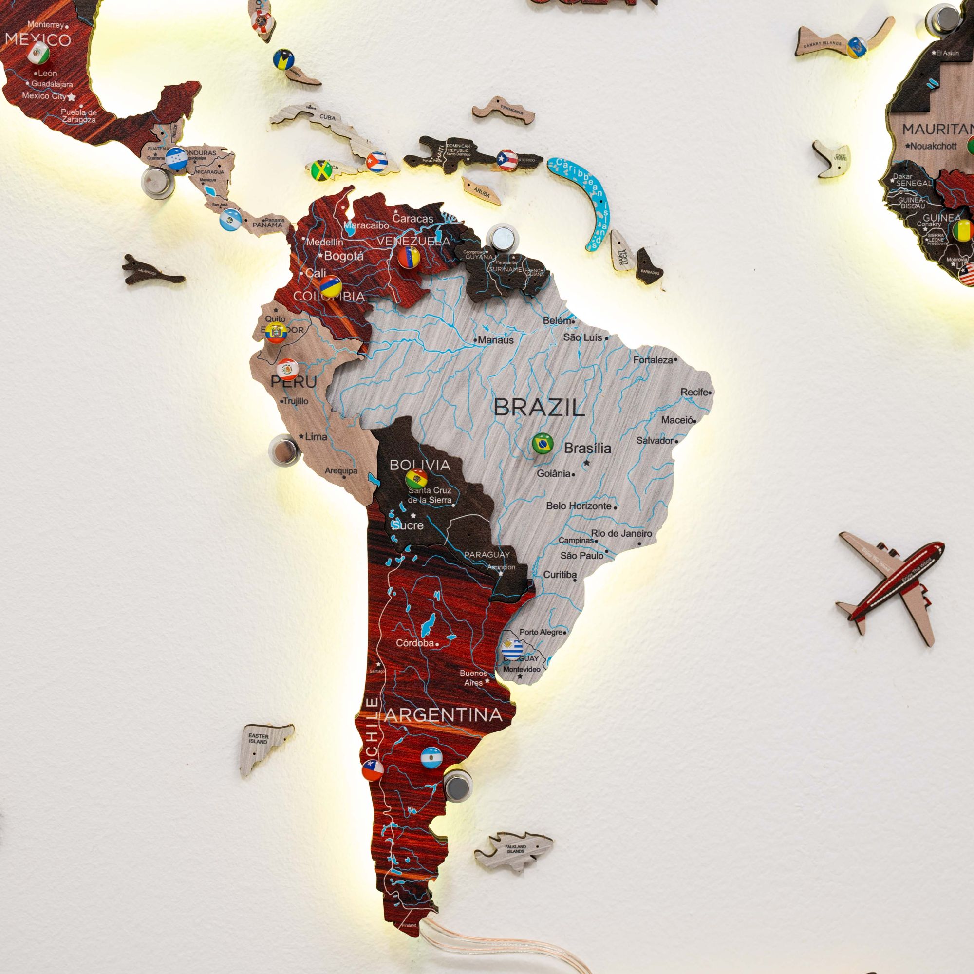 Wooden map of South America with various countries and an airplane icon on a white background.