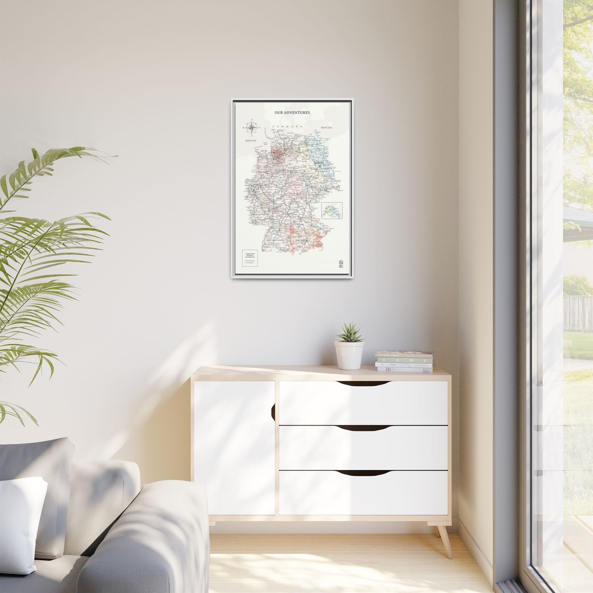 Modern interior with a white dresser, framed map, and plant.