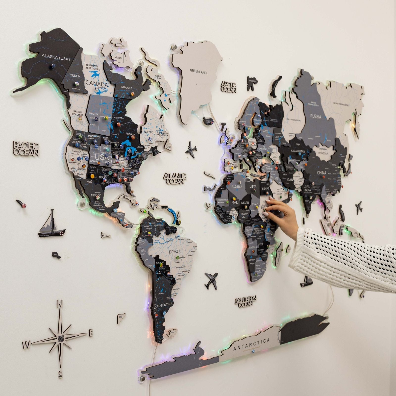 World map with LED lights on a white wall, showing a hand placing a marker.