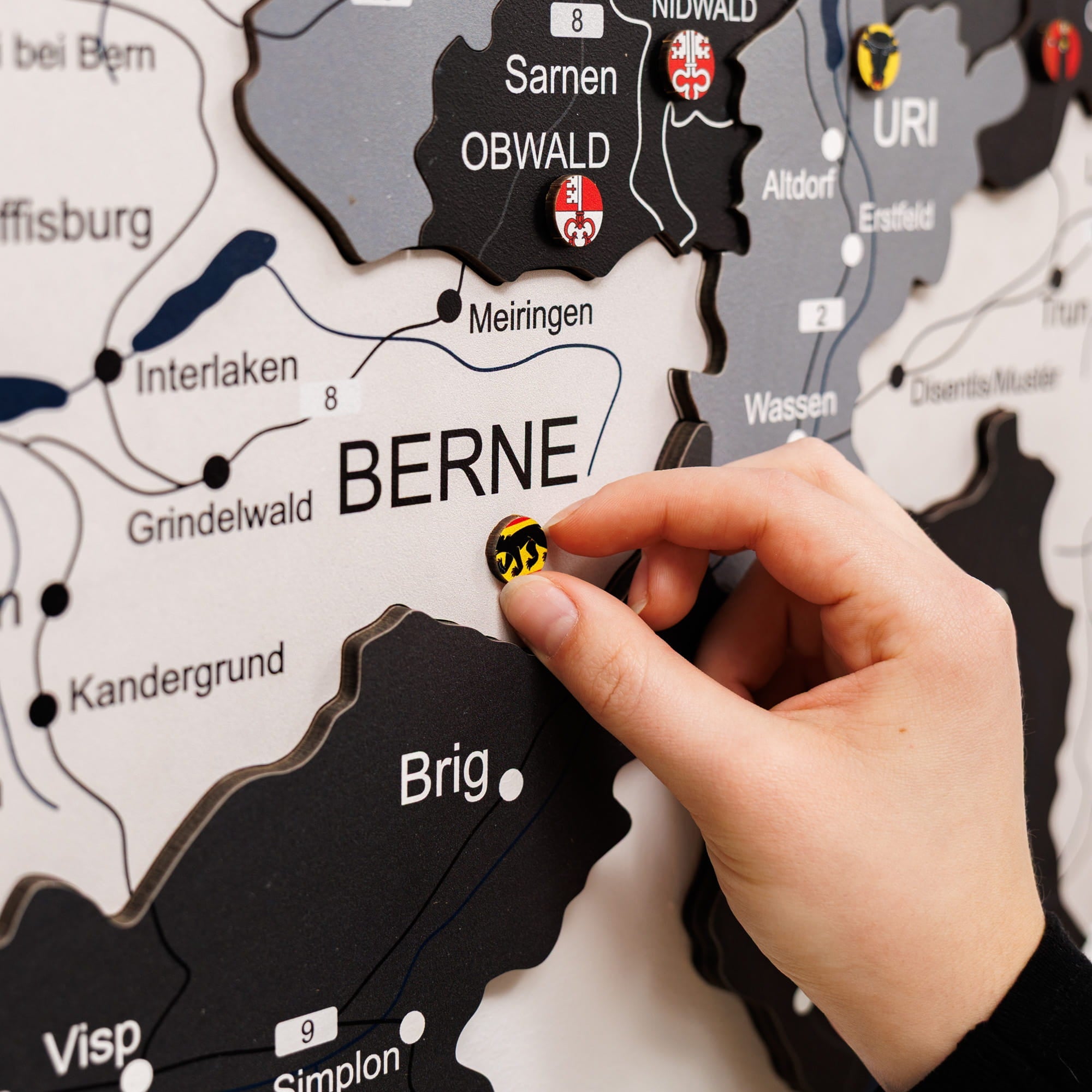 Hand placing a magnet on a map of Switzerland, focusing on Bern.