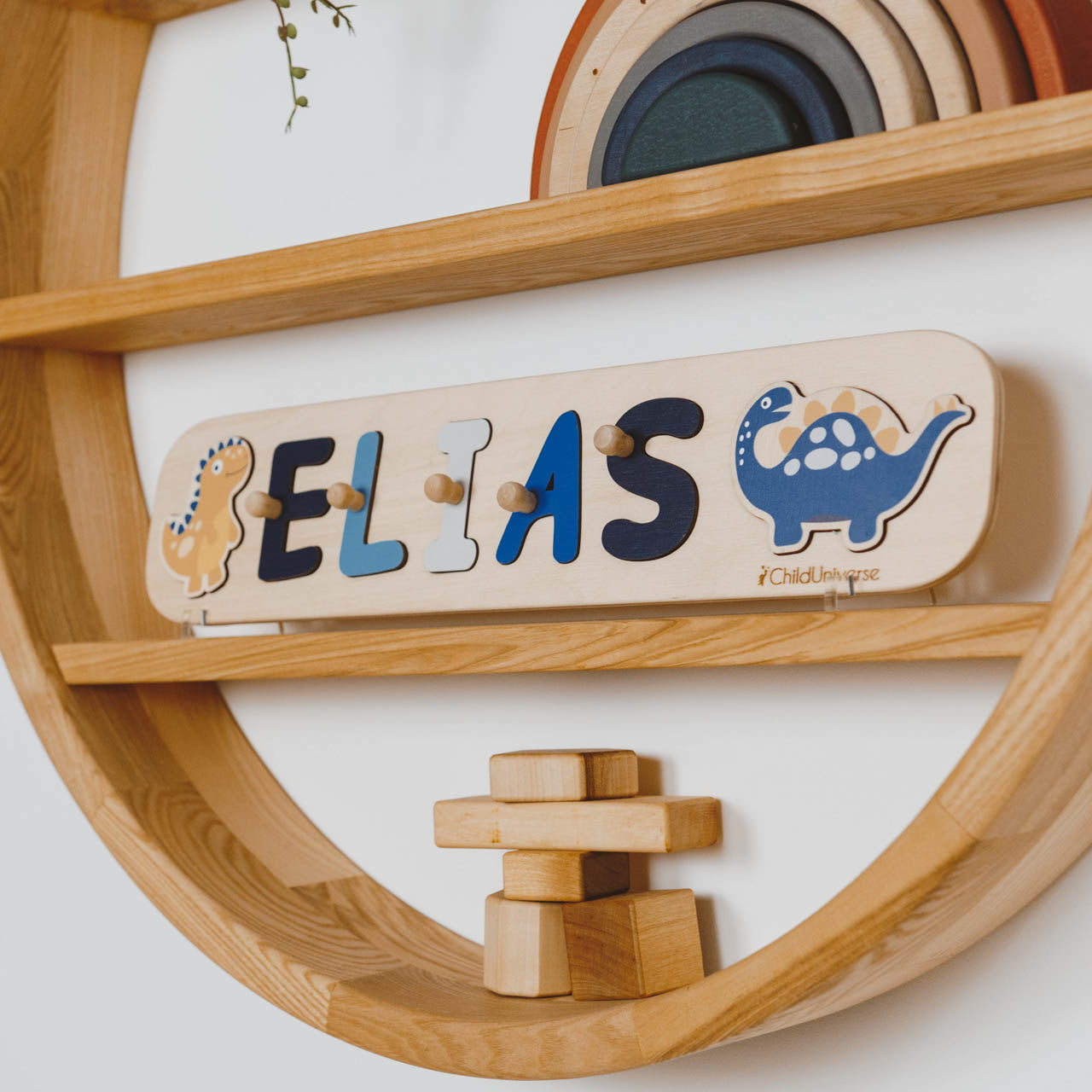 Wooden name plaque with 'ELIAS' and dinosaur designs on a wooden shelf.