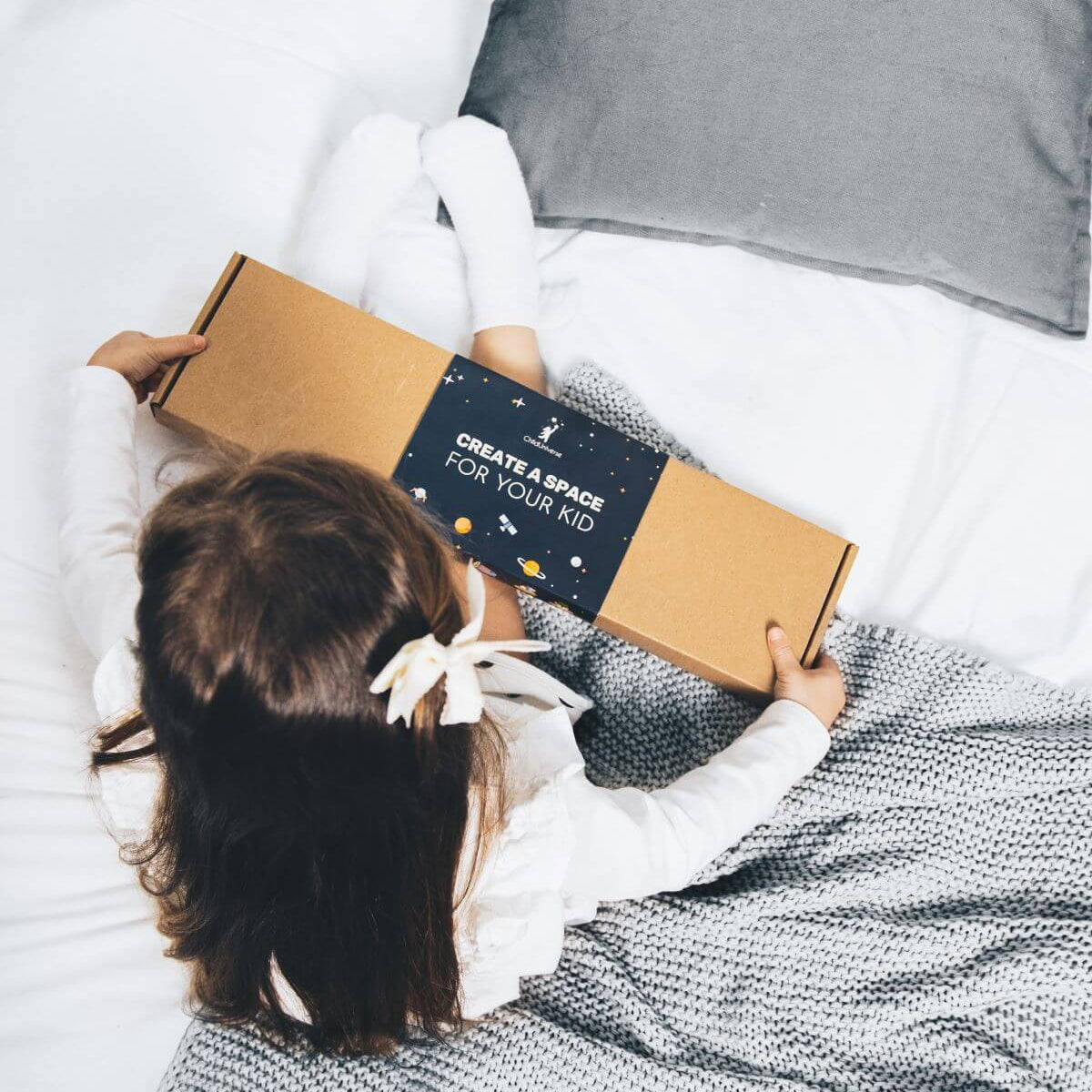 Child holding a cardboard box with a label on a bed