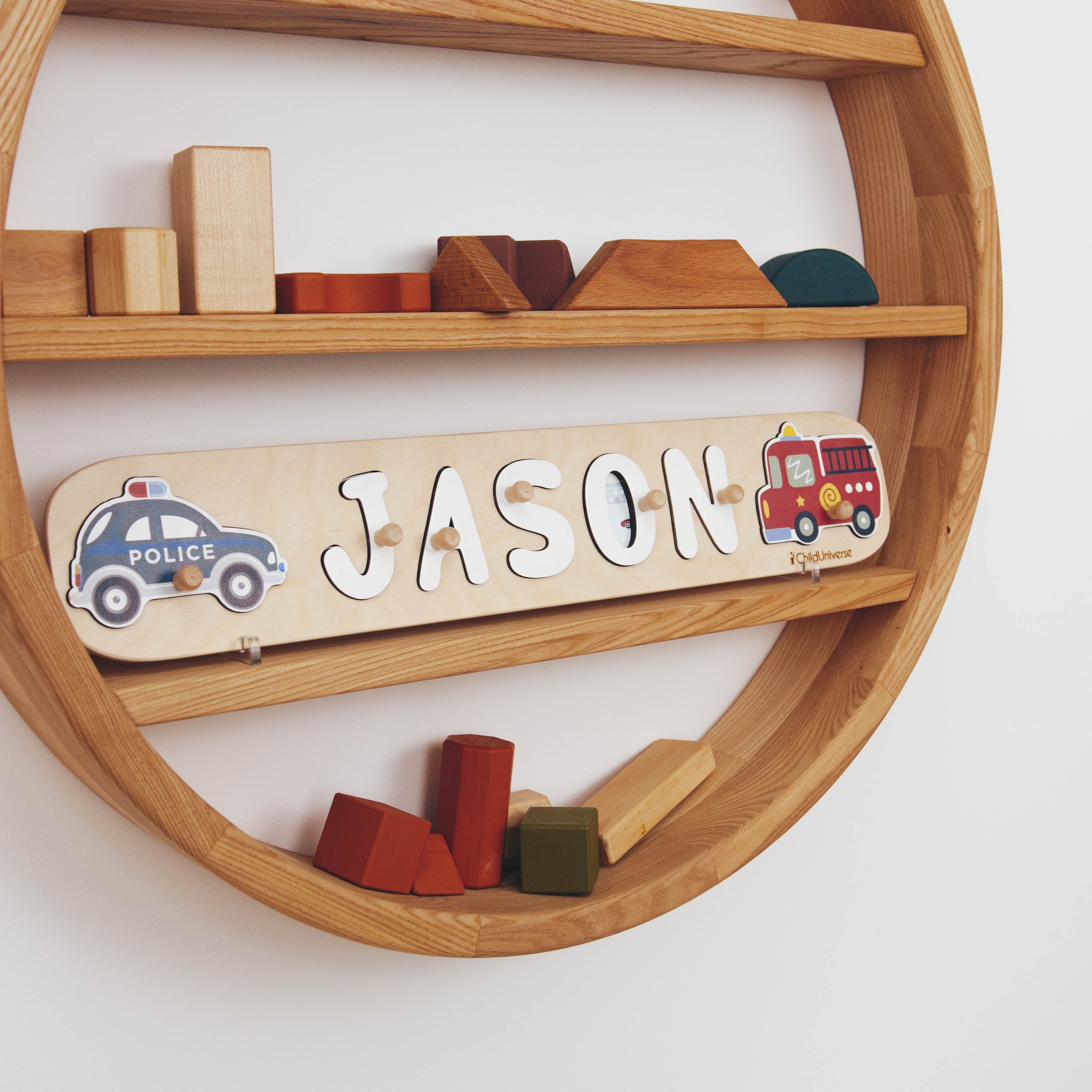 Wooden nameplate with 'JASON' and illustrations of a police car and fire truck on a wooden shelf.
