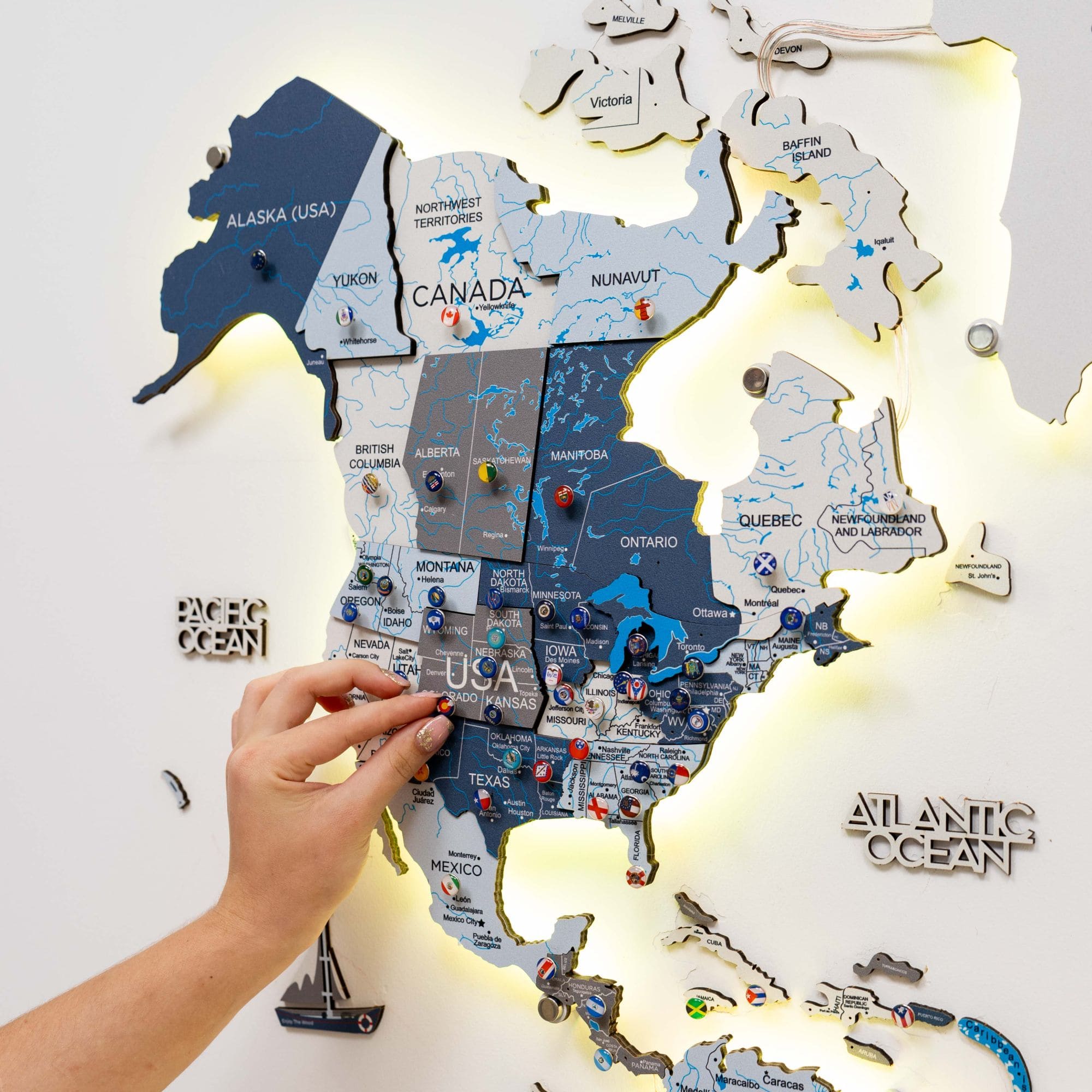 Lighted wall map of North America with a hand placing a piece.