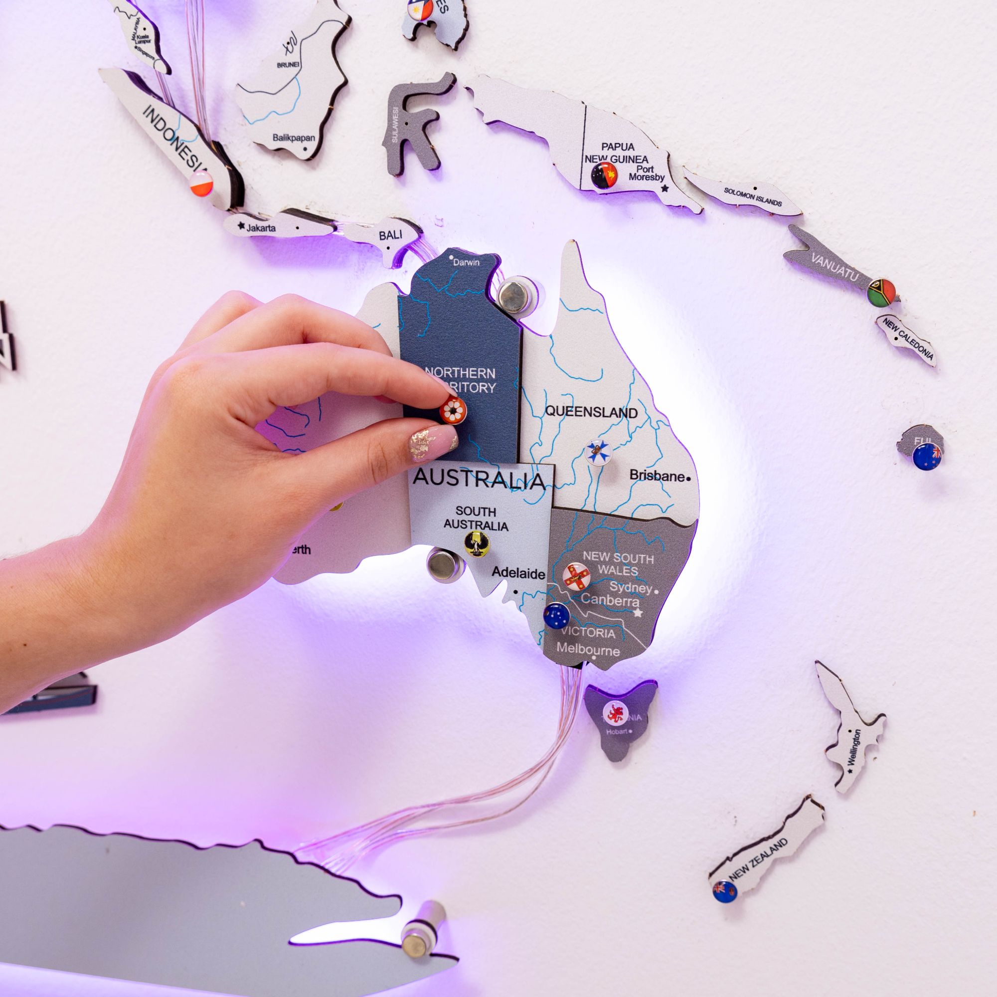 Hand holding a card labeled 'Australia' on a map-themed light-up board with various country names.