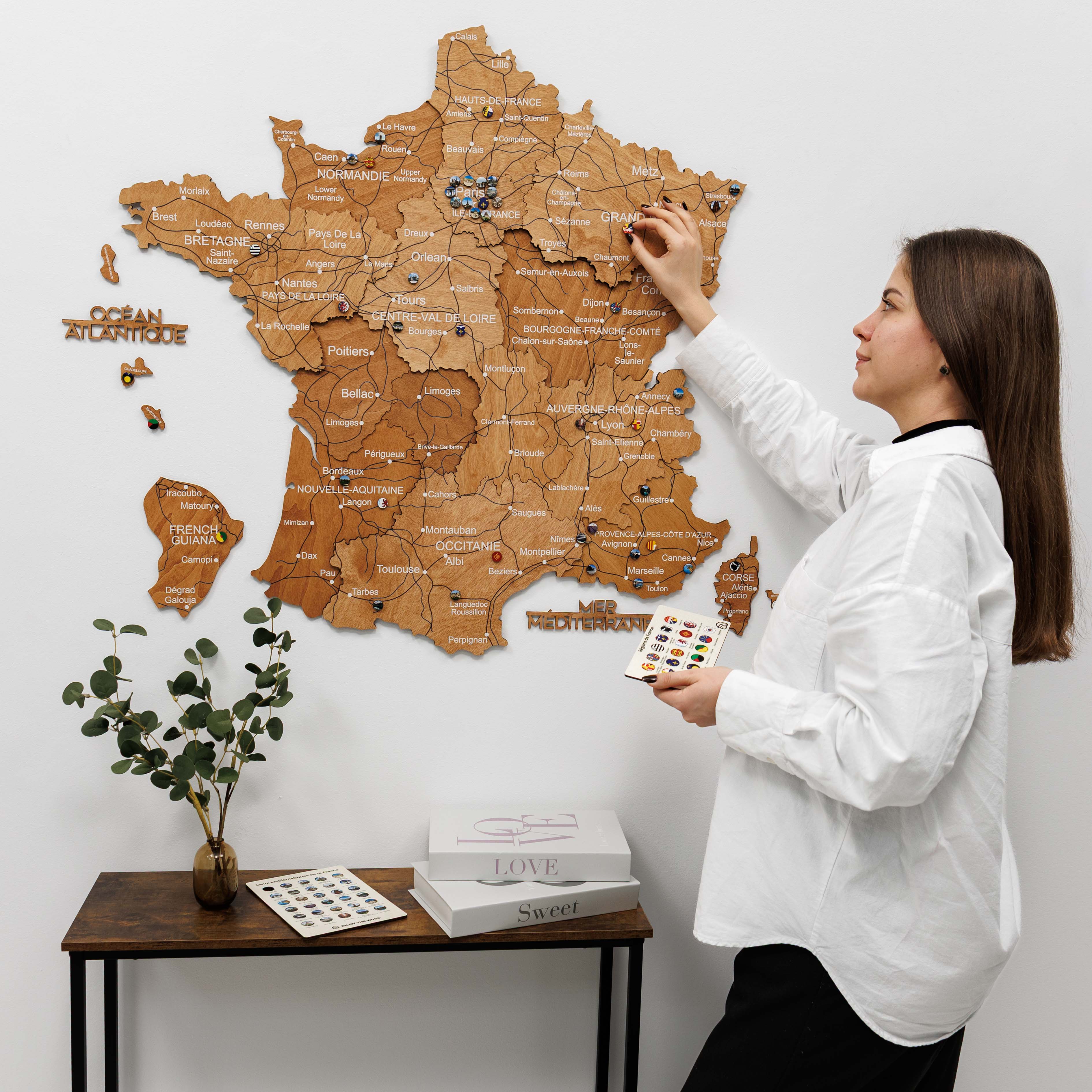 Woman interacting with a wooden map of France on a white wall.