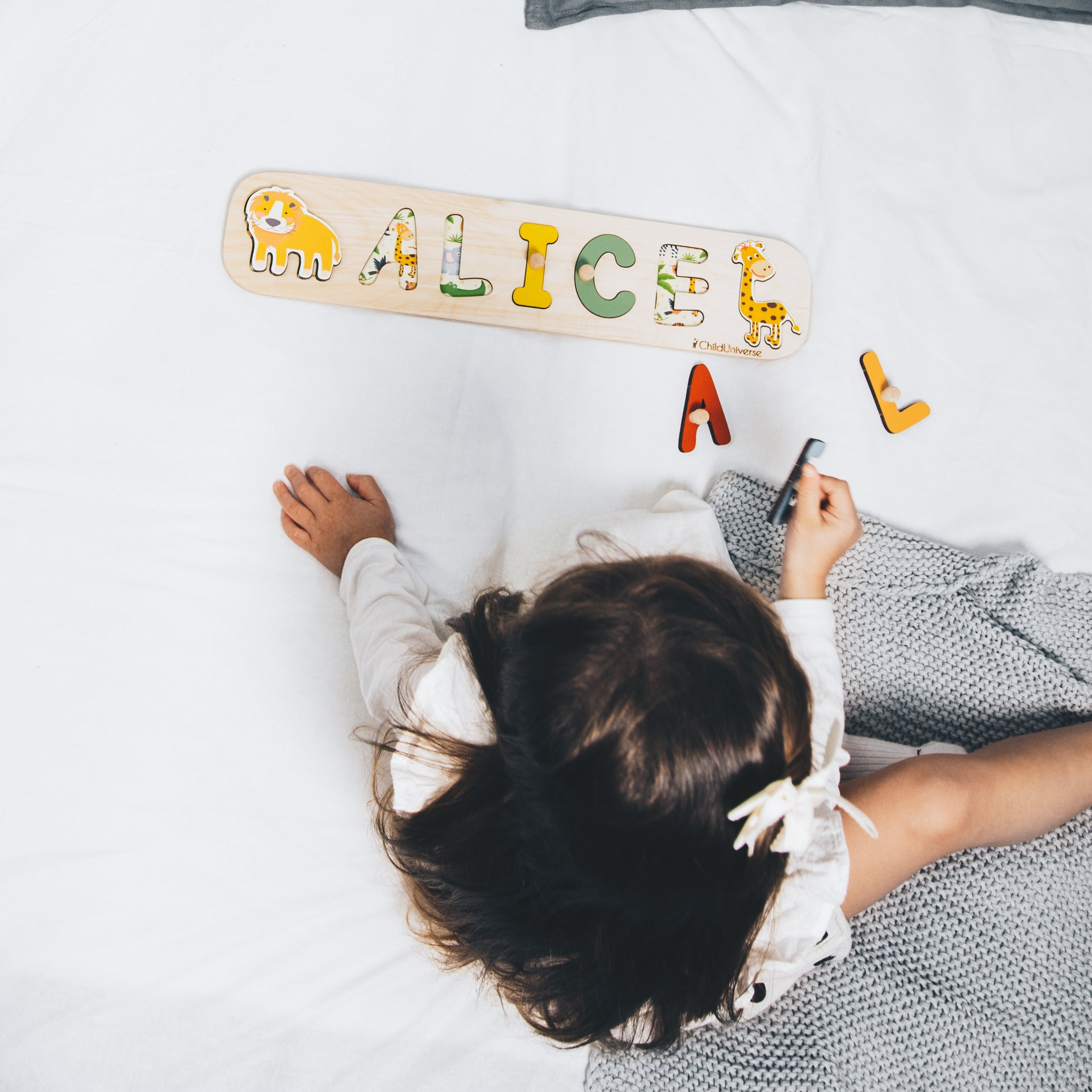 Child playing with wooden letters spelling 'ALICE' on a bed