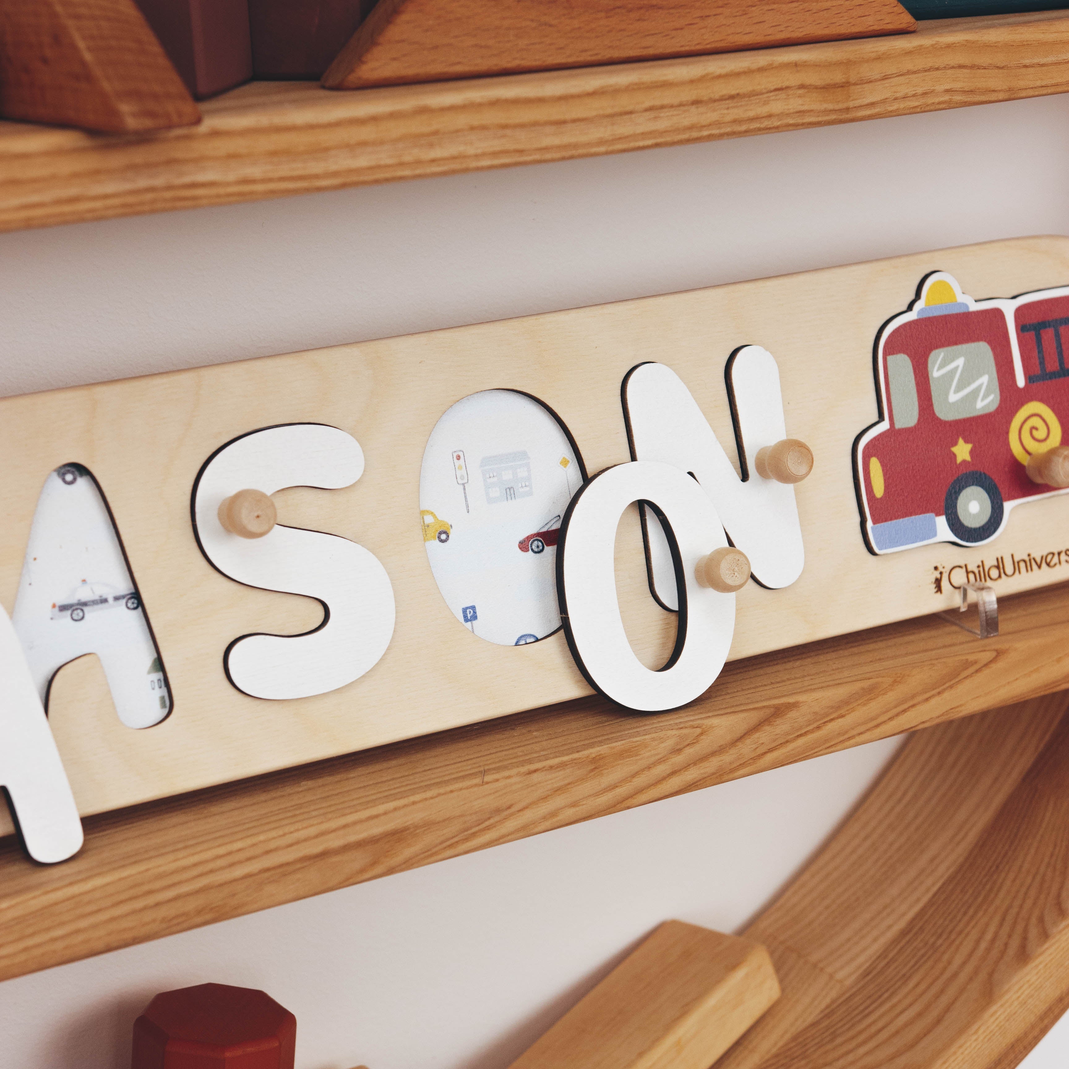 Wooden name sign with 'MASON' and a fire truck, on a wooden shelf with toys.