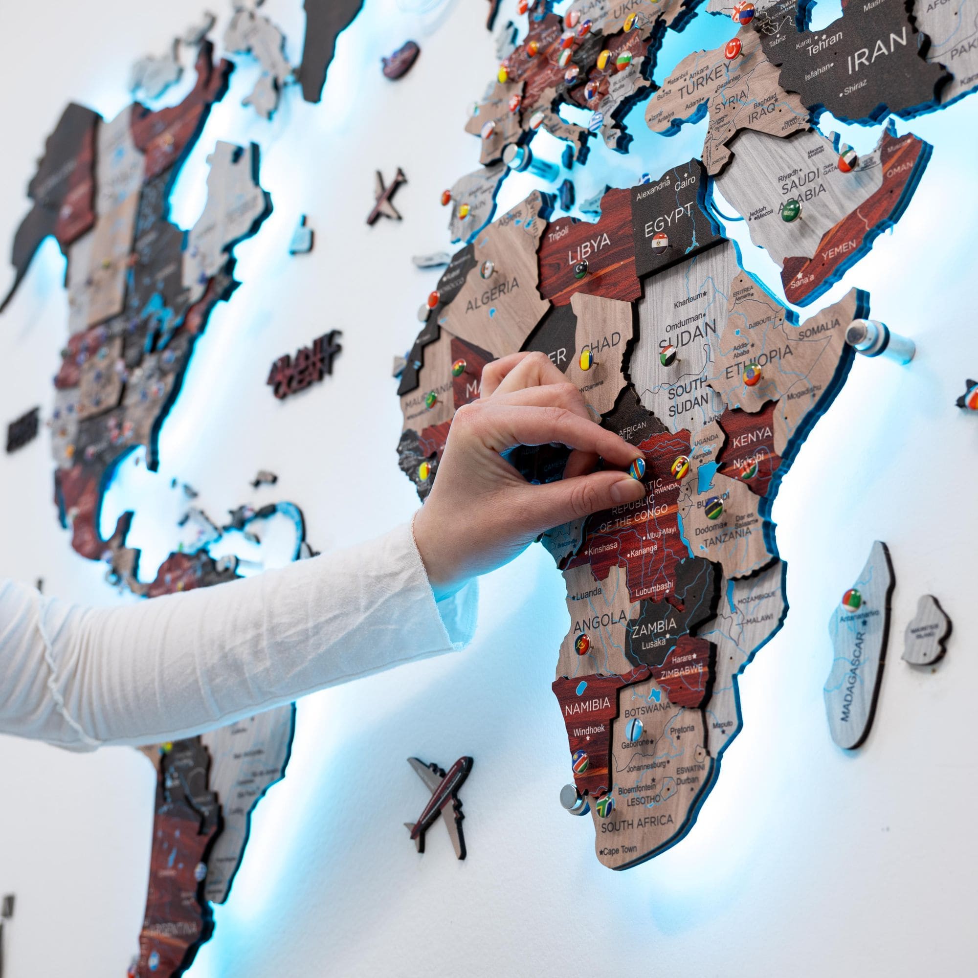 Hand placing a pin on a wooden world map with illuminated background
