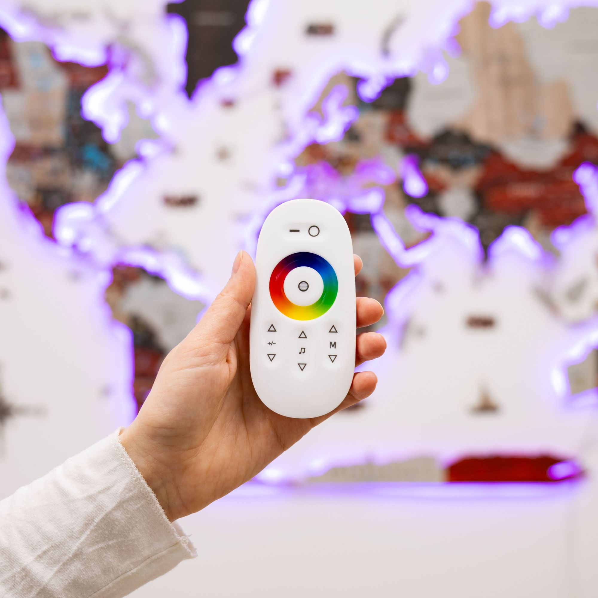 Hand holding a white remote control with color wheel design in front of a blurred indoor background.